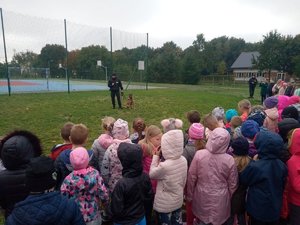 Boisko szkolne. Policjant wraz z psem rozmawia z uczniami.