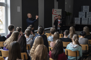 Policjant prowadzi prelekcję dla uczniów w sali konferencyjnej.