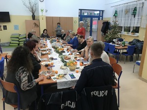 Uczestnicy spotkania siedzący przy stole. Wśród nich policjant.