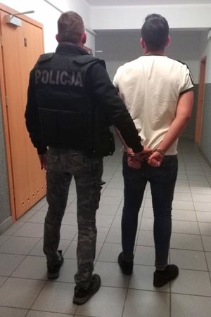 policjant trzyma zatrzymanego zakutego w kajdanki