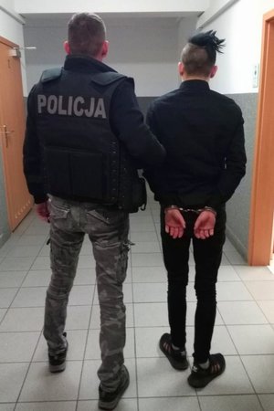 policjant trzyma zatrzymanego zakutego w kajdanki