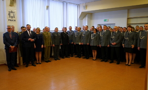 Goście i policjanci uczestniczący w uroczystości stojący w szeregu.