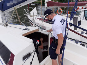 Policjant stojący na jachcie podczas kontroli instalacji przez strażaka wewnątrz jachtu.