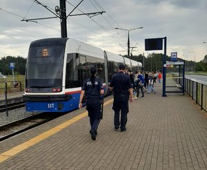 Policjanci idą w stronę tramwaju stojącego na przystanku.