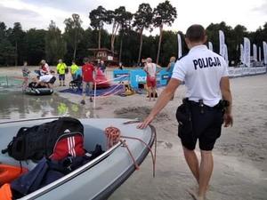 Policjant stoi przy policyjnej łodzi na brzegu akwenu.