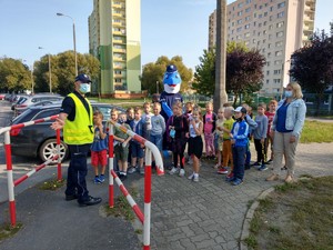 Policjanci z dziećmi przy przejściu dla pieszych. Wśród dzieci stoi polfinek.