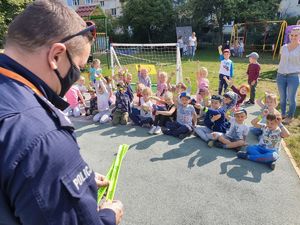 Policjant stoi przed dziećmi trzymając odblaski.