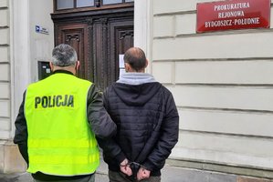 policjant prowadzi zatrzymanego skutego kajdankami