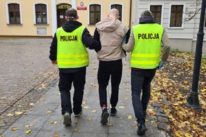 dwaj policjanci prowadzą zatrzymanego skutego kajdankami założonymi na ręce trzymane z tyłu