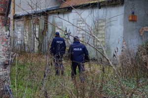 Policjanci idący przez zarośla do miejsca przebywania osób bezdomnych.