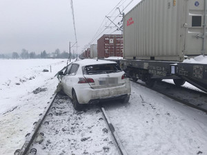 uszkodzony biały peugeot stoi na torach, a obok stoją wagony