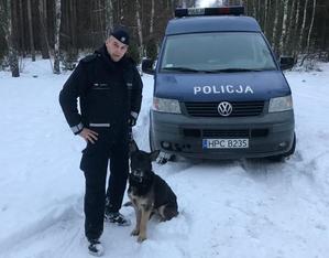 Policjant z Fioną w lesie. Zimowa sceneria. Za nimi stoi policyjny radiowóz.