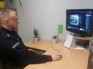 Policjant siedzi przy biurku przed komputerem podczas zajęć online.