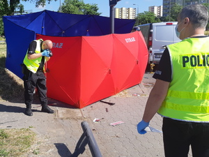 Policjant fotografuje ślady na miejscu wypadku. w tle parawan osłaniający ofiarę wypadku.