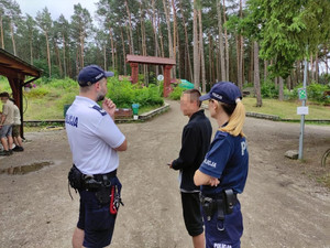 Policjanci rozmawiają z mężczyzną w terenie leśnym.