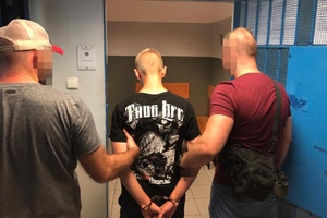 dwaj policjanci trzymają mężczyznę skutego kajdankami