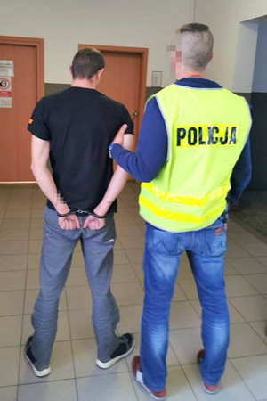 policjant trzyma zatrzymanego skutego kajdankami