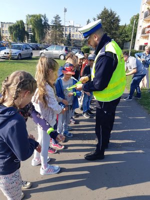 Policjant rozdaje uczniom odblaski i zakłada je na rękę.