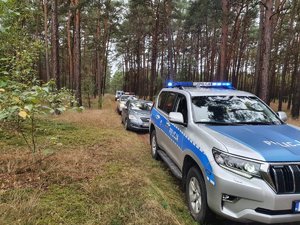 Kilka radiowozów zaparkowanych jeden za drugim na drodze leśnej.