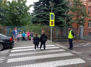 Uczniowie przechodzą przez przejście dla pieszych pod okiem policjanta.