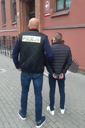 policjantka trzyma zatrzymanego skutego kajdankami