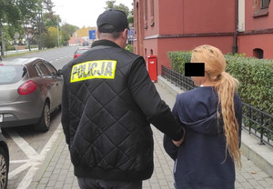 policjant trzyma zatrzymaną skutą kajdankami