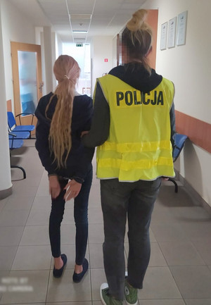 policjantka trzyma zatrzymaną skutą kajdankami