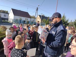 policjant rozdaje dzieciom ulotki z wizerunkami pojazdów służb ratunkowych