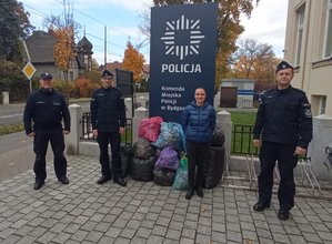 Policjanci stoją przed bydgoską komendą. Obok nich leżą worki z nakrętkami.