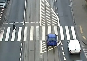 Kierowca niebieskiego pojazdu osobowego przejeżdża przez przejście dla pieszych nie ustępując pieszemu znajdującemu się na przejściu dla pieszych.