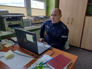 Policjant siedzi przy biurku podczas zajęć online z uczniami.