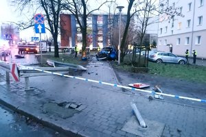 niebieska rozbita mazda stoi na chodniku koło drzew, obok stoją umundurowani policjanci