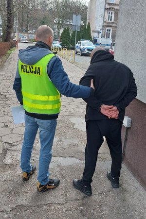 policjant trzyma zatrzymanego skutego kajdankami