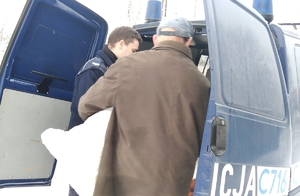 Policjant i mężczyzna stoją przy otwartej strefie ładunkowej radiowozu.