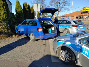 niebieska skoda uderzyła w ogrodzenie w krzewy. Auto ma otwarty bagażnik. Obok stoi policjant, a za nim stoją dwa oznakowane radiowozy