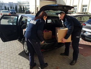 Policjanci pakują kartony z darami do bagażnika samochodu.