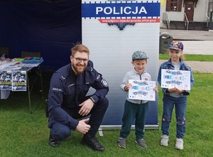 Policjant kuca przy dwojgu dzieci trzymających kolorowankę.