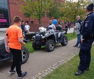 Dziecko siedzi na policyjnym quadzie. Obok stoi policjant i inne osoby.