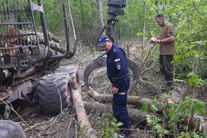 policjant i strażnik leśny stoją przy maszynie do wycinki drzew