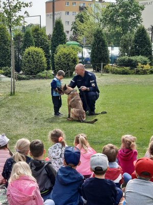 Policjant z psem oraz chłopiec stoją przed grupą dzieci.