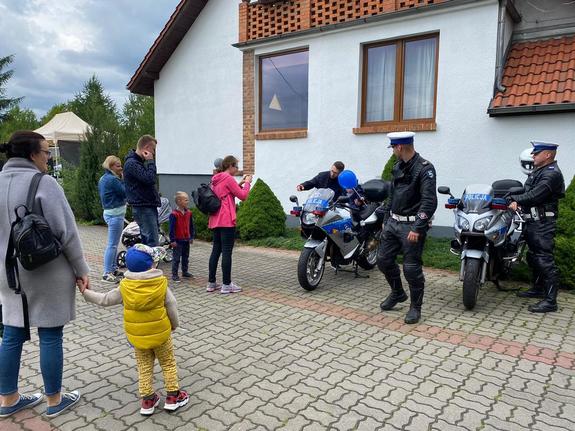 Policjanci przy motocyklach policyjnych zaparkowanych w miejscu odbywania się festynu. Obok nich dzieci i dorośli.