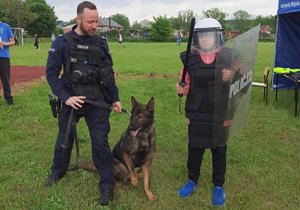 policjant z psem służbowym stoi obok chłopca ubranego w policyjny sprzęt