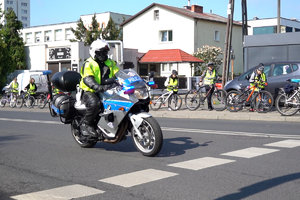 policjant na motocyklu jedzie ulicą. w oddali na chodniku dzieci prowadzą rowery
