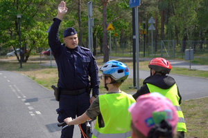 policjant unosi rękę do góry. Dzieci na rowerach się przyglądają