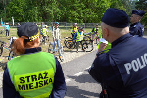 strażniczka miejska i policjant patrzą na dzieci na rowerach