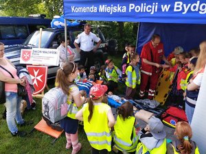 dzieci stoją przed stoiskiem, gdzie pokazywana jest pierwsza pomoc przez Maltańską Służbę Medyczną