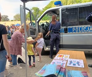 Dzieci i dorośli stoją przy radiowozie policyjnym.