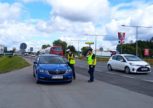 Policjanci ruchu drogowego kontrolują niebieski samochód osobowy.
