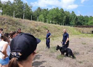 Policjanci z psem służbowym na strzelnicy rozmawiają z uczestnikami pikniku.