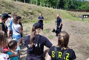 Policjanci z psem służbowym rozmawiają z osobami zgromadzonymi na strzelnicy.